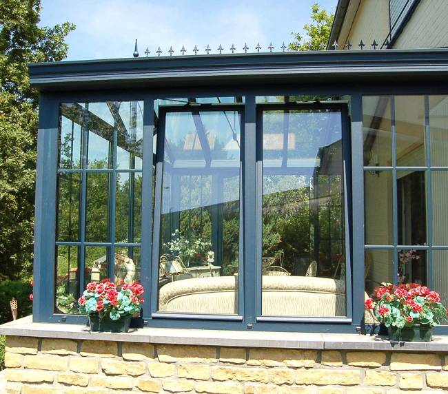 Elegant aluminium tilt and turn windows with classic grid design, complementing the stone facade and outdoor flower decor.