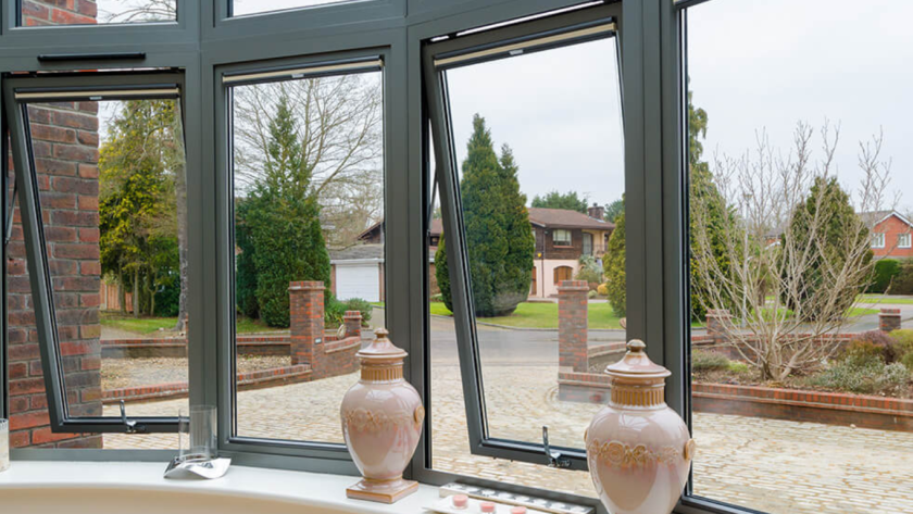 Open aluminum double glazed windows framing a cozy living room view of a charming country house yard