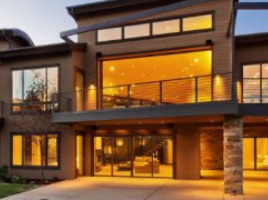 Modern home exterior with large bronze aluminium windows and warm interior lighting, featuring anodised finish.