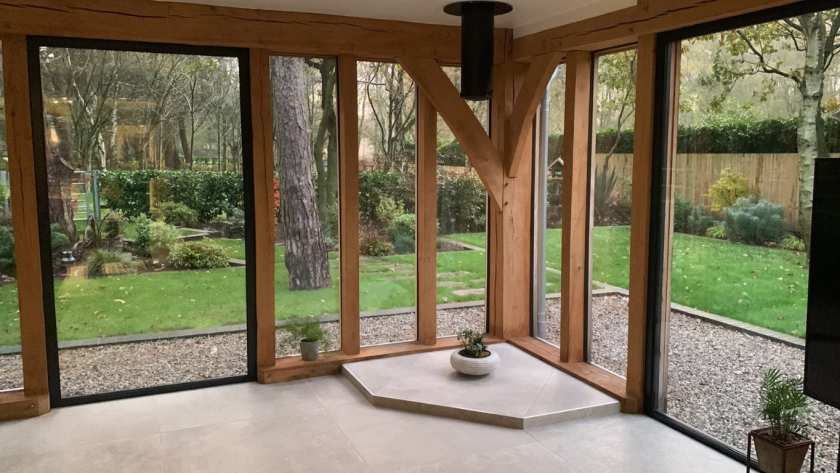 Room with floor-to-ceiling aluminium brown windows and wooden frames overlooking a landscaped garden.