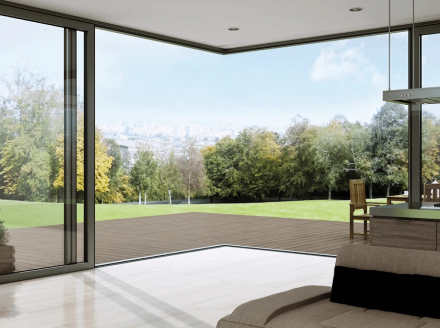 Panoramic view through aluminium corner window overlooking a spacious wooden deck and green landscape with trees and distant city skyline.