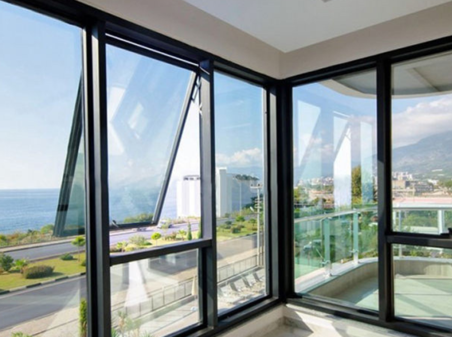 View through modern European aluminium windows in a corner room, overlooking a coastal road, sea, and distant mountains under a bright sky