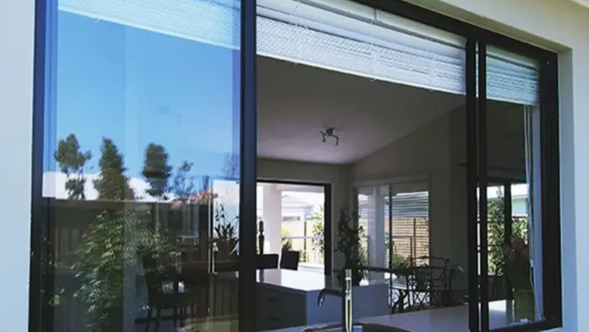 Kitchen view through large aluminium frame glass window with clear exterior reflections