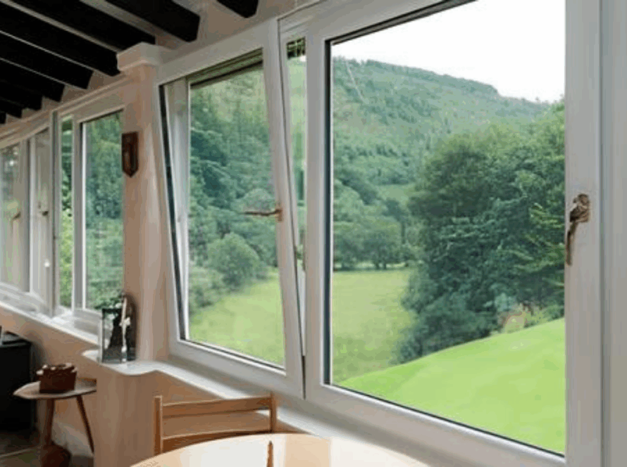 Outward opening tilt and turn windows installed in a cozy living room overlooking a lush green landscape