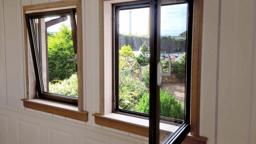 Two tilt and turn windows in a wooden frame, one in tilt mode and one in turn position, overlooking a landscaped garden