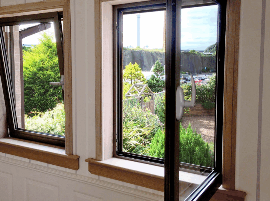 Two tilt and turn windows in a wooden frame, one in tilt mode and one in turn position, overlooking a landscaped garden