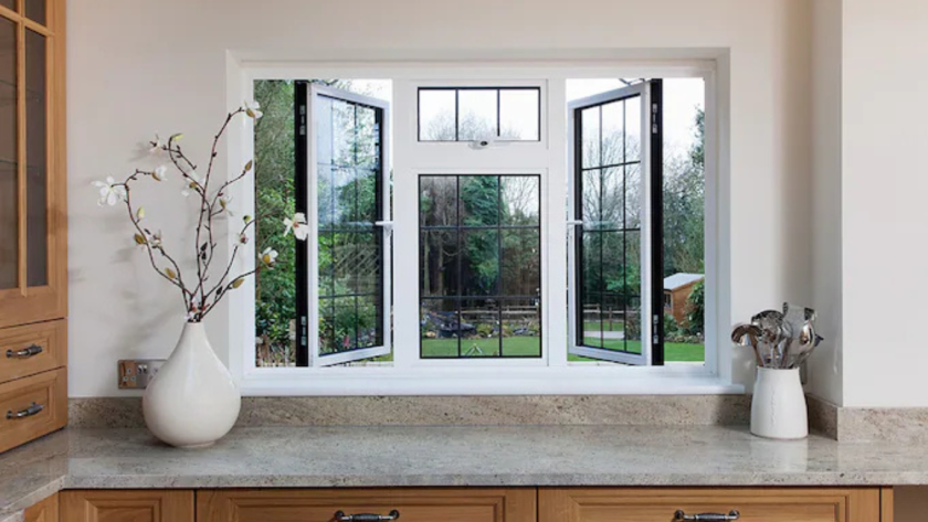 Kitchen interior with open white aluminium windows and classic white window frames overlooking a green backyard.