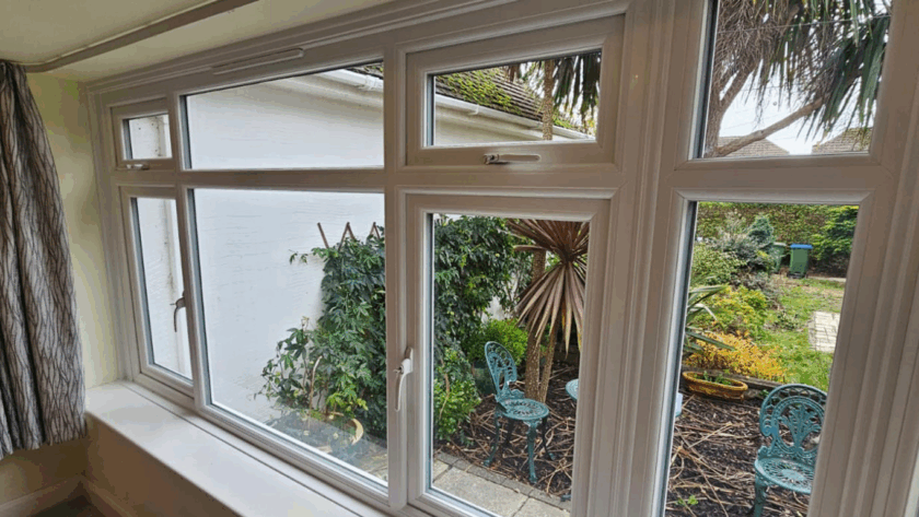White casement glass window overlooking a cozy garden with outdoor seating