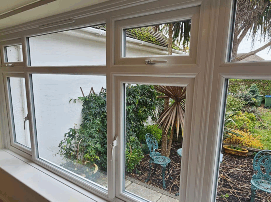 White casement glass window overlooking a cozy garden with outdoor seating