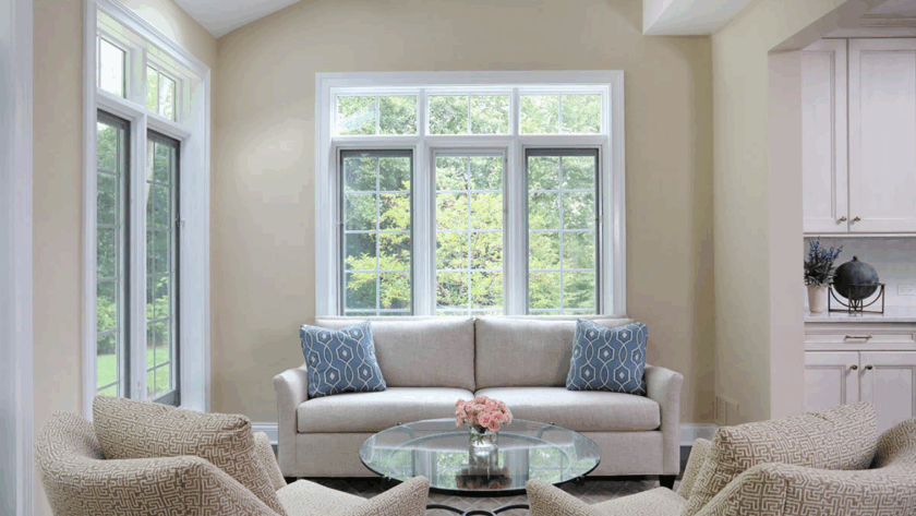 Bright living room with casement transom windows, neutral furniture, and a view of lush greenery