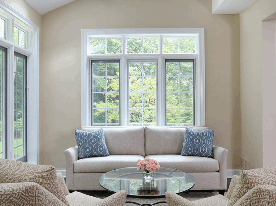 Bright living room with casement transom windows, neutral furniture, and a view of lush greenery