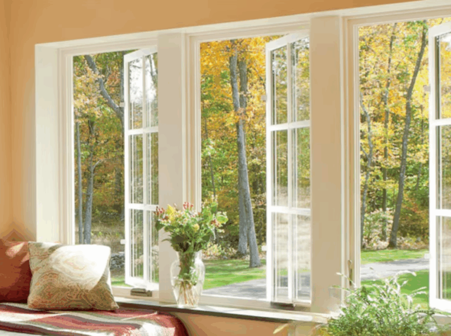 White casement windows open wide, filling a cozy room with autumn light, framed by soft orange walls, pillows, and fresh flowers on a windowsill
