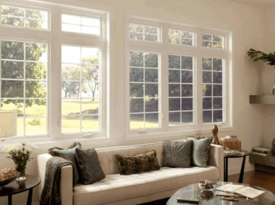 White casement windows with decorative grids, enhancing a bright, elegant living room interior overlooking lush greenery