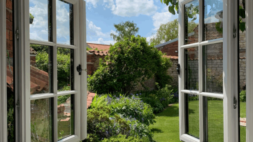 White double casement windows opened wide, overlooking a charming garden on a sunny day