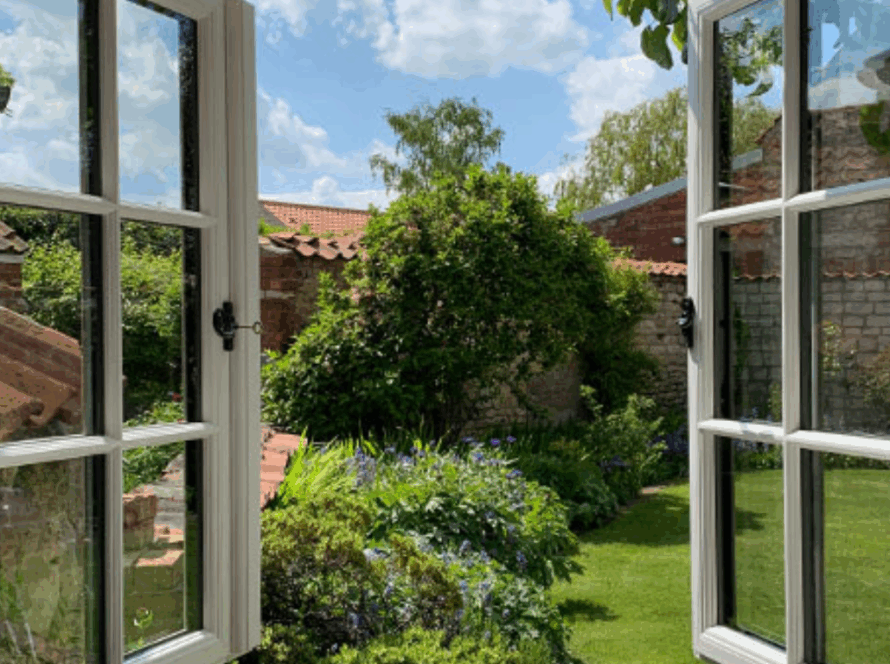 White double casement windows opened wide, overlooking a charming garden on a sunny day