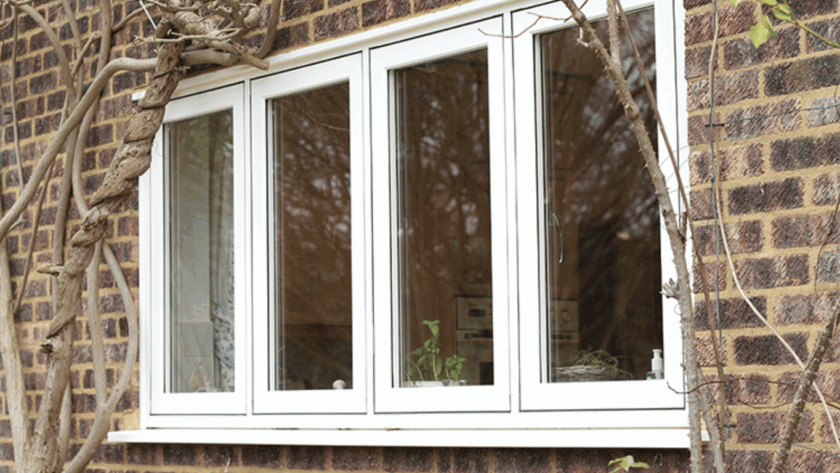 White flush windows installed in a brick exterior wall, surrounded by climbing branches, offering a seamless, modern finish