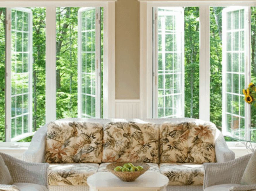 Bright living room with large white vinyl casement windows opened outward, surrounded by greenery, sofa and sunflowers in foreground