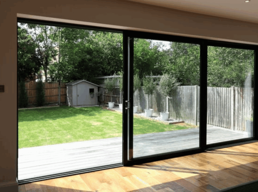 Three-panel sliding window revealing a green backyard and wooden deck