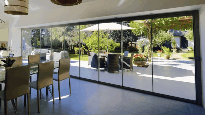 Frameless sliding glass window overlooking a garden patio with outdoor seating and greenery