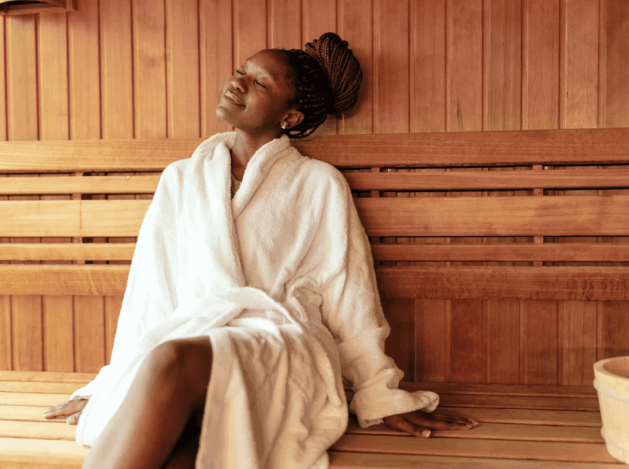 Woman relaxing in a wooden sauna wearing a bathrobe, enjoying heat therapy and wellness session