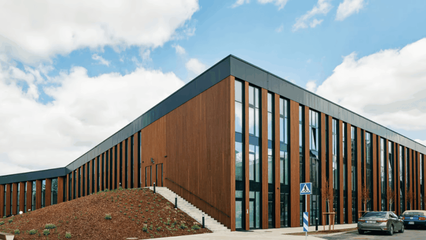 Modern commercial building with vertical thermowood cladding, large glass windows, and a minimalist architectural design under a blue sky.