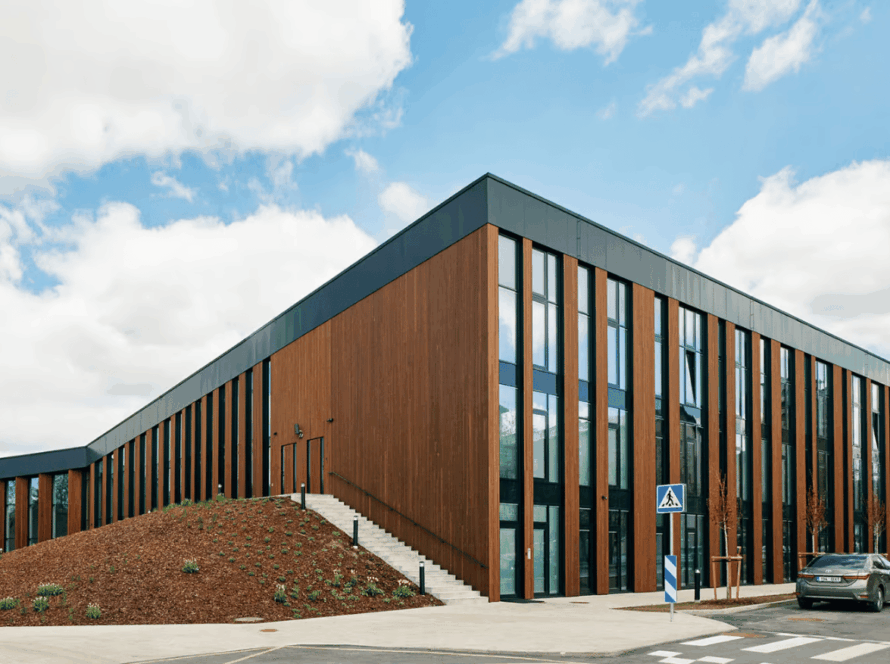 Modern commercial building with vertical thermowood cladding, large glass windows, and a minimalist architectural design under a blue sky.