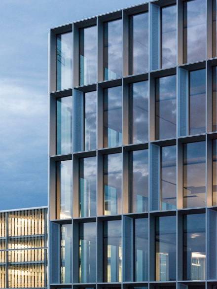 Modern building elevation featuring a curtain wall system with deep aluminum profiles and reflective glazing, emphasizing geometric precision and contemporary design.