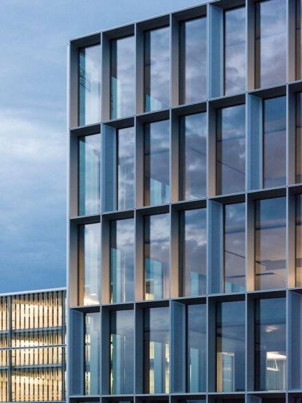 Modern building elevation featuring a curtain wall system with deep aluminum profiles and reflective glazing, emphasizing geometric precision and contemporary design.
