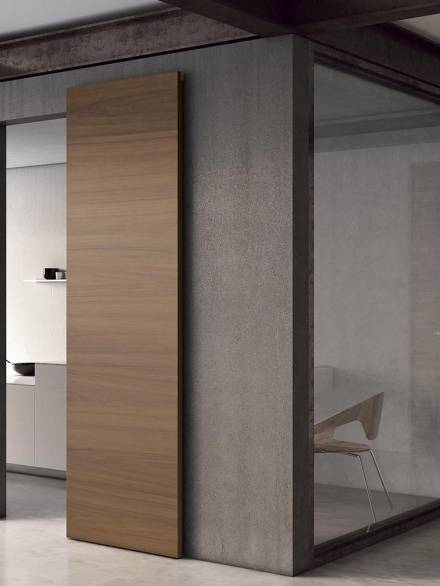 Minimalist interior with a wooden sliding door mounted on a dark frame, adjacent to a glass-walled office space.