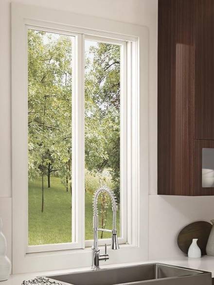 Aluminium sliding windows with a white frame installed above a kitchen sink, opening to a green, tree-filled view.