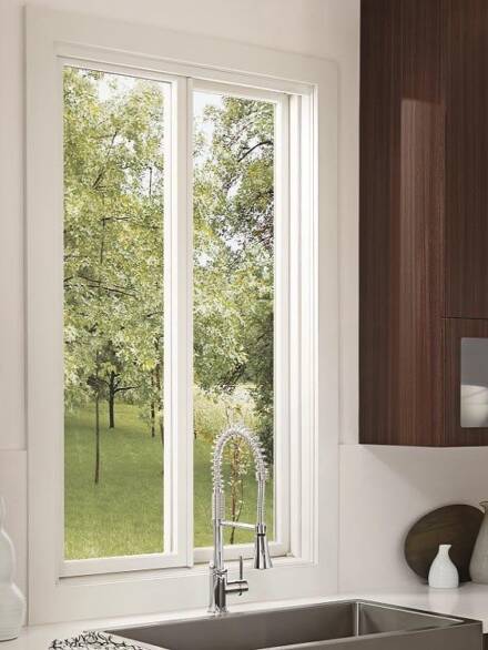 Aluminium sliding windows with a white frame installed above a kitchen sink, opening to a green, tree-filled view.