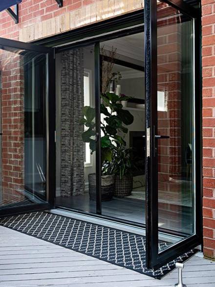 Aluminium swinging doors with a sleek black frame, opening onto a wooden deck and allowing natural light to flow into the interior living space.