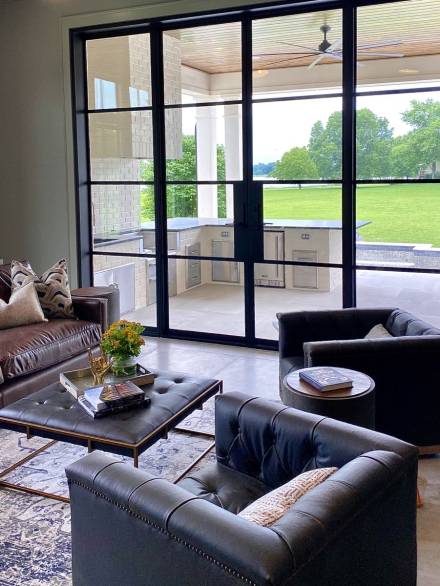 ce9d0e6fc5f57e5517d91093fb7e895c Modern patio doors with sleek black aluminum frames and large glass panels seamlessly connect a cozy living area to a spacious outdoor kitchen and a vibrant green lawn.