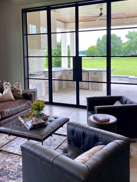 Modern patio doors with sleek black aluminum frames and large glass panels seamlessly connect a cozy living area to a spacious outdoor kitchen and a vibrant green lawn.