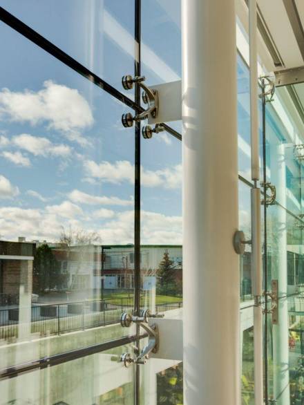 Close-up view of a planar glazing system showcasing stainless steel spider fittings that secure large glass panels to the structural framework, allowing maximum transparency and a sleek, frameless aesthetic.