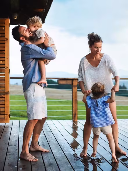 family-plays-on-deck Happy family enjoying time together on a wet wooden deck with scenic countryside views in the background.