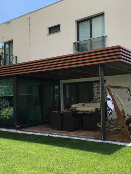 Modern winter garden extension with dark-framed glazing and a wooden ceiling, offering a shaded and stylish outdoor living area.