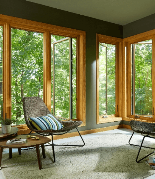 Casement aluminium windows with natural wood interiors bringing in forest views to a cozy reading nook.