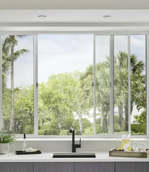 sim_interior_6200_kitchen_3_lite_sliding_window_5050_module_carousel_1_p111182 Aluminium sliding windows above a kitchen sink, providing a clear view of lush greenery and palm trees.