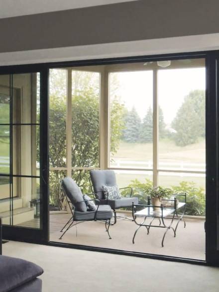 Elegant winter garden with black aluminium sliding doors, seamlessly connecting the indoor lounge with a sunlit outdoor patio.